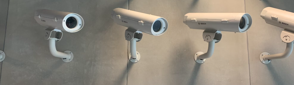 Vier wandgemonteerde beveiligingscamera's op rij op een grijze ondergrond voor verbeterde bedrijfsbeveiliging.