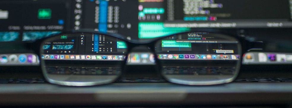 Brillen gericht op de voorgrond met wazige computerschermen met SEO-code op de achtergrond.