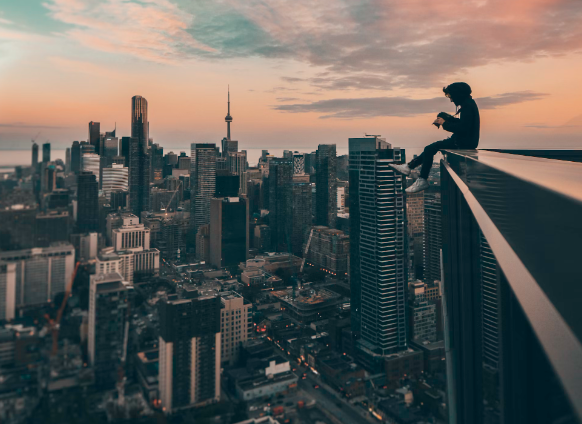 Persoon die op de rand van een hoog gebouw zit en naar een tablet kijkt met de skyline van de stad en een zonsondergang op de achtergrond, terwijl hij een SEO-strategie beoordeelt.