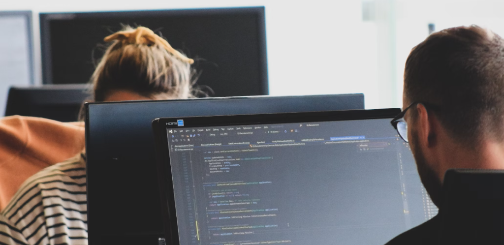 Twee mensen werken op computers in een kantoor en bekijken de cyberbeveiligingscode op een van de schermen.