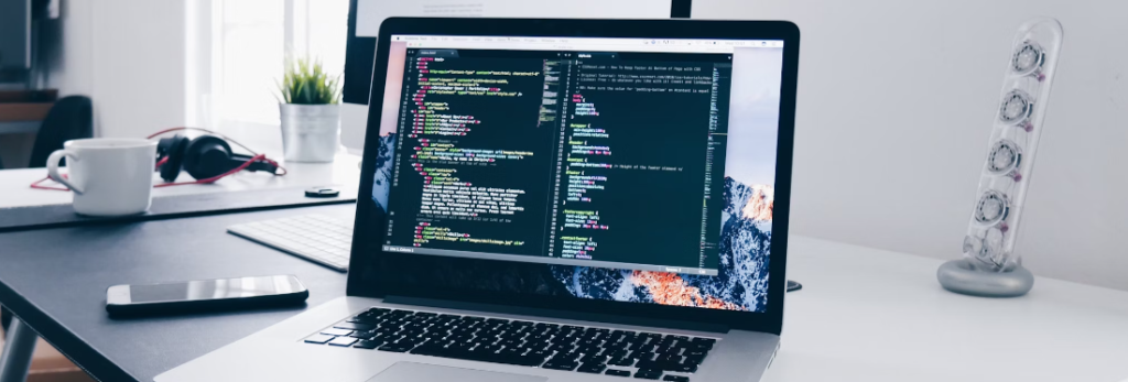 Laptop op een bureau met AWS-code, met koptelefoon en een decoratief spiraalvormig notitieblok aan de zijkant in een moderne kantooropstelling.