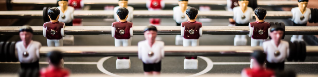 Close-up van tafelvoetbalspelers, met figuren in witte en rode uniformen gemonteerd op metalen staven, klaar voor een intense simulatie van de tegenstander.