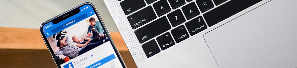 Een smartphone met een Facebook-profiel ligt op een tafel naast het toetsenbord van een MacBook, stilletjes naast de drukke activiteiten van een Security Operations Center.