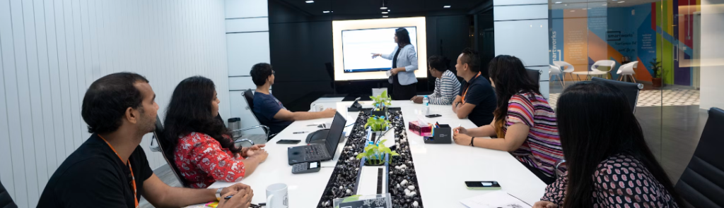 Een diverse groep cybersecurityprofessionals in een moderne vergaderruimte, aandachtig luisterend naar een presentator die naar een scherm wijst.