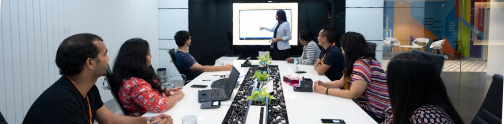 Iemand geeft een presentatie over het Incident Response Plan aan een groep van zes personen, zittend rond een vergadertafel in een moderne kantooromgeving.