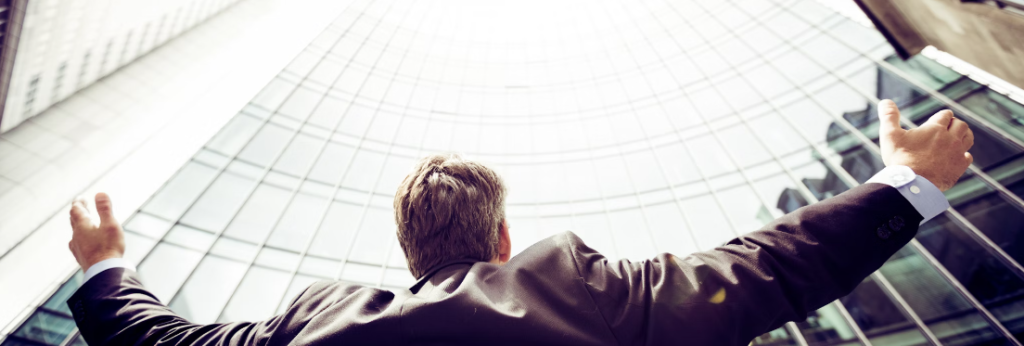 Een man in een pak staat triomfantelijk met opgeheven armen in het cybersecurity-operatiecentrum van een stedelijke, glazen bouwomgeving.