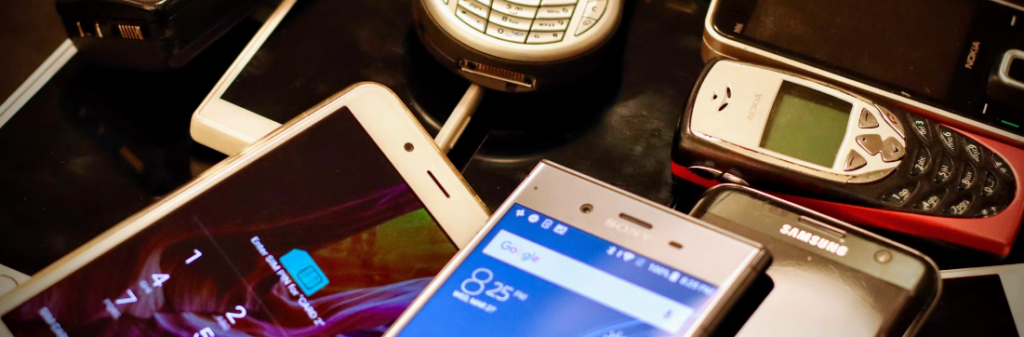 Een verzameling oude en nieuwe mobiele telefoons, waaronder een Nokia en een Samsung, tentoongesteld op een donker oppervlak, met de top 10 cyberbeveiligingstrends voor 2024.