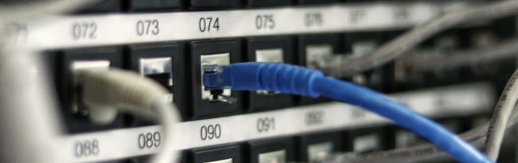 Een blauwe ethernetkabel aangesloten op een beveiligde poort op een netwerkswitch, terwijl andere onbezette poorten en kabels op de achtergrond zichtbaar zijn.