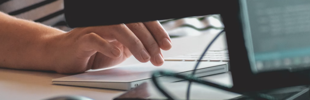 Close-up van de hand van een persoon die op een toetsenbord typt met een computermonitor op de achtergrond met een beveiligde poort.