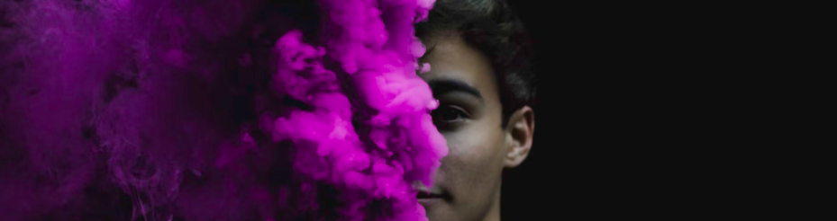 Het gezicht van een persoon wordt gedeeltelijk verduisterd door een wolk van levendige paarse rook tegen een donkere achtergrond, waardoor een raadselachtig en boeiend beeld ontstaat. Voor de beste tips over navigeren door cloudbeveiliging hoeft u niet verder te zoeken.