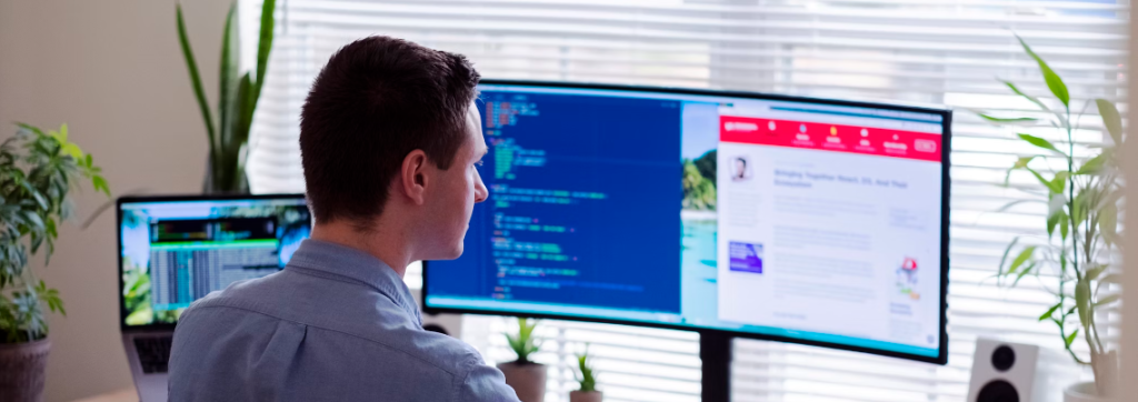 Een persoon die aan een bureau werkt met drie computermonitoren, waarvan er één code weergeeft, de andere een webpagina en de derde een terminal. De kamer is goed verlicht en er komt natuurlijk licht binnen via zonwering, waardoor een ideale werkruimte ontstaat waar u zich kunt concentreren op cyberbeveiligingstaken binnen hun digitale ecosysteem.