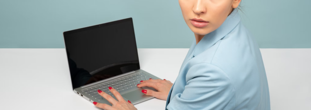 Een vrouw in een blauwe blazer typt op een laptop terwijl ze over haar schouder kijkt en wellicht een Incident Response Plan doorneemt.