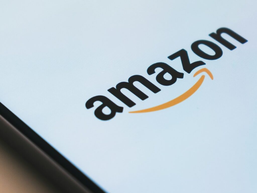 Close-up van het Amazon-logo weergegeven op een scherm, met de naam van het bedrijf met een gebogen pijl die lijkt op een glimlach onder de letters 'am' en 'on', wat de verreikende diensten symboliseert, waaronder AWS en cyberveiligheid.