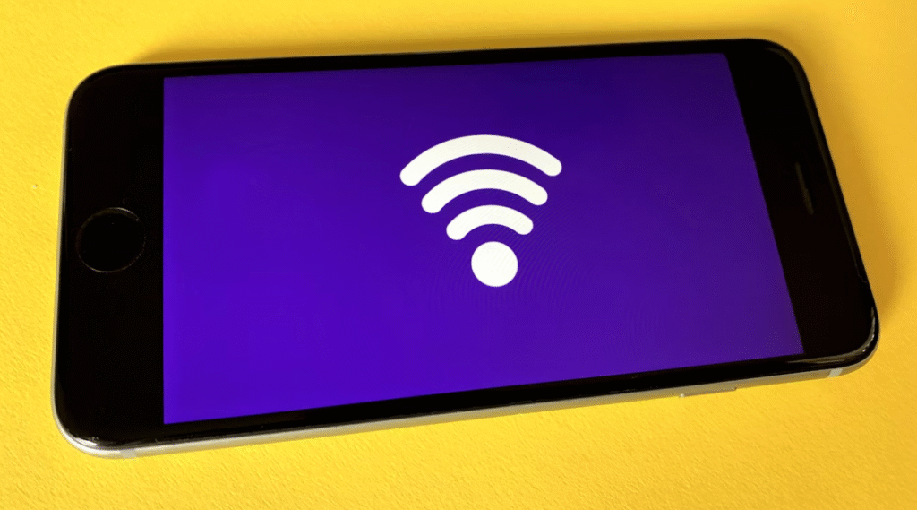 Een smartphone met een groot wit wi fi symbool op een paars scherm, geplaatst op een geel oppervlak om gebruikers te herinneren aan de beveiliging van wifi wanneer ze verbinding maken met openbare netwerken.